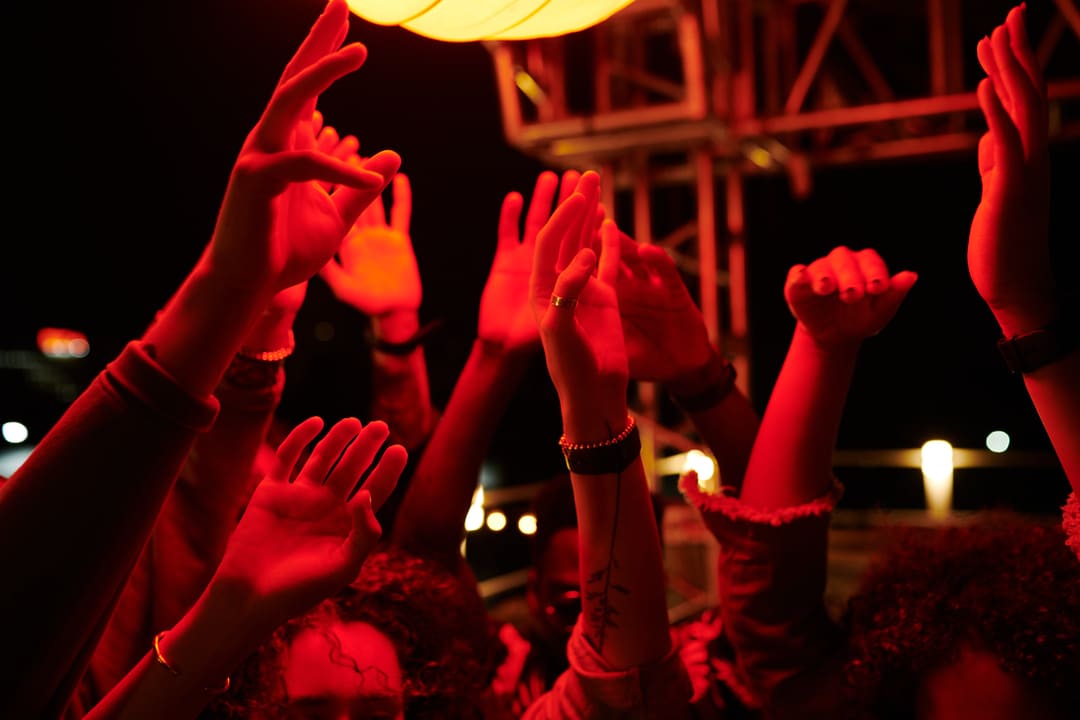 Pessoas jogam as mãos para o alto com uma luz vermelha iluminando o ambiente.